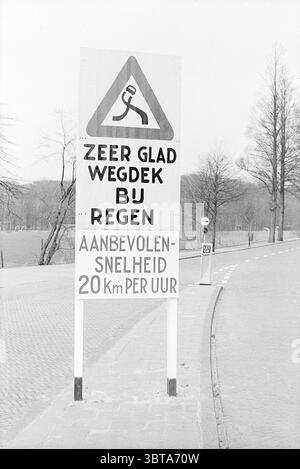 Panneau '20 km' Heemstede Signs, Whizgle News, Dutch Desk, pays-Bas, 1950 - 2000 le 13-03-1968. L'image contient ces rubriques. La scène présente un grand panneau debout bien en vue à côté d'une route. Le panneau est conçu pour transmettre des informations importantes, avec une forme de mise en garde triangulaire en haut, soulignée par un fond jaune. À l’intérieur du triangle, il y a une silhouette noire qui suggère de la prudence ou de la vigilance, représentant probablement une personne glissant. La partie inférieure du panneau fournit des détails supplémentaires dans un format clair et gras, mettant l'accent sur les conditions glissantes, en particulier lorsque Banque D'Images