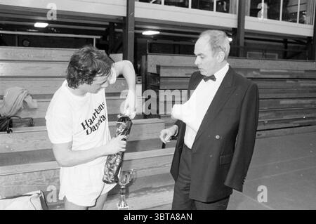 Adieu à Paul Onkenhout Cup présentation par Michael van Praag Haarlems Dagblad etc. et IJmuider courant et Koeri, Whizgle News, Dutch Desk, pays-Bas, 1950 - 2000 on 24-02-1990. Ces rubriques apparaissent dans l'image. Dans un cadre intérieur, deux hommes sont engagés dans la conversation. Un homme, vêtu de vêtements de sport décontractés, semble présenter quelque chose d'une bouteille. Il a un comportement jeune, et sa tenue reflète une ambiance sportive avec un t-shirt qui se démarque de son short blanc. Son expression suggère de l'enthousiasme ou de l'empressement. L'autre homme est vêtu de vêtements habillés, avec un Banque D'Images