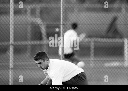 Tennis : Jansen - Van Beek Santpoort Santpoort, Whizgle News, Dutch Desk, pays-Bas, 1950 - 2000 le 22-08-1993. L'image montre ces rubriques. Dans cette scène, un homme est accroupi, concentré intentionnellement alors qu'il interagit avec une balle ronde, se préparant peut-être à la lancer ou à la lancer. Il porte une chemise à manches longues de couleur claire associée à un short sombre, contrastant avec la toile de fond monochrome. Son front est sillonné, suggérant la concentration, tandis que son corps est positionné près du sol, indiquant un moment actif. En arrière-plan, une autre figure est visible, légèrement floue, suggérant un mouvement an Banque D'Images