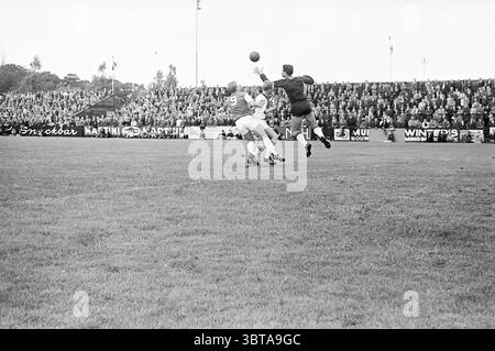 RCH - Ajax Football, Whizgle News, Dutch Desk, pays-Bas, 1950 - 2000 le 18-08-1963. Ces rubriques sont illustrées dans l'image. Au premier plan, deux athlètes sont engagés dans un moment dynamique d'un match de football. Un joueur, vêtu d'un maillot blanc et d'un short, saute dans les airs pour intercepter une balle haute, présentant une expression déterminée. L'autre joueur, portant un maillot de couleur foncée, semble tenter de bloquer ou de contester la capture, son attention étant évidente lorsqu'il s'étire vers le haut. Autour d'eux, sur le terrain de jeu herbeux, le vert éclatant de l'herbe contraste fortement avec le Mo Banque D'Images