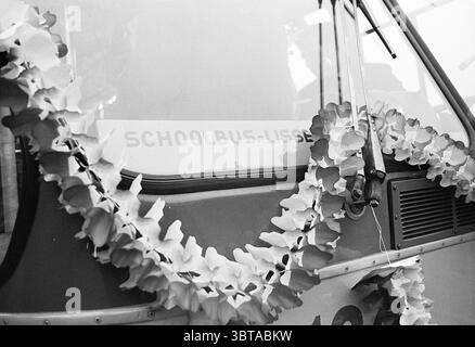 1er bus scolaire lisse Noord Zuid Hollandse Vervoersmaatschappij N.V. NZ, Whizgle News, Dutch Desk, pays-Bas, 1950 - 2000 on 20-01-1969. L'image contient ces rubriques. La scène présente un autobus scolaire vintage lumineux, mis en évidence avec une surface brillante et polie reflétant la lumière ambiante douce. Son devant est orné d'une délicate guirlande de fleurs artificielles, créant un contraste saisissant avec la peinture métallique du bus. Les fleurs, dans les tons crème et jaune pâle, sont disposées de manière fluide, drapant élégamment sur le devant. Le bus lui-même a un orange chaud et silencieux Banque D'Images