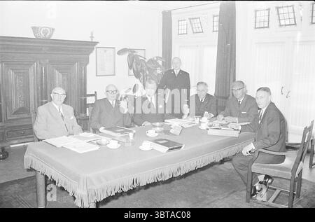 B. et W. Velsen avec Messenger et sans Messenger conseils municipaux, Whizgle News, Dutch Desk, pays-Bas, 1950 - 2000 le 26-06-1962. Ces rubriques sont illustrées dans l'image. La scène montre un groupe de huit hommes rassemblés autour d'une grande table rectangulaire. Le cadre semble être un bureau ou une salle de réunion formelle, caractérisé par son mobilier et son décor sophistiqués. La table est recouverte d'une nappe sombre qui a une frange le long de ses bords. Divers documents et dossiers sont dispersés dans la table, indiquant une réunion sérieuse en cours. Au centre, petit café blanc Banque D'Images
