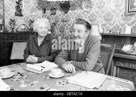 M. Braam auteur d'un livre à IJmuiden avec sa femme à la table dans le salon IJmuiden pays-Bas, Whizgle News, Dutch Desk, pays-Bas, 1950 - 2000 le 08-02-1985. Voici les rubriques de l'image. Dans une pièce chaleureusement décorée, deux personnes s'assoient à une table ornée d'une nappe à motifs floraux. Les couleurs de la nappe sont douces, donnant une douce chaleur au décor. La table est sertie de tasses délicates, suggérant un moment de thé ou de café, ajoutant à l'atmosphère accueillante. D'un côté, une femme âgée avec les cheveux blancs bouclés et un comportement gentil porte un Banque D'Images
