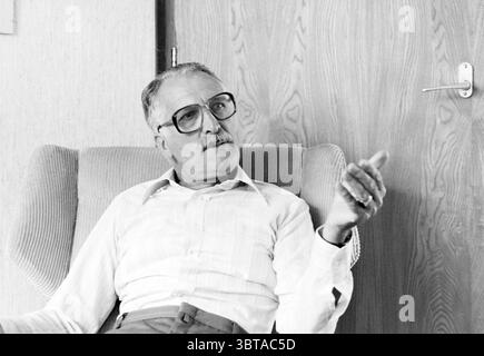 Portrait Mr. Voogt Haarlem personnes Haarlem pays-Bas, Whizgle News, Dutch Desk, pays-Bas, 1950 - 2000 le 25-06-1982. L'image inclut ces rubriques. Dans la scène, un homme est assis confortablement dans un grand fauteuil moelleux. Il a une apparence distinguée, caractérisée par ses lunettes et une expression réfléchie. Il fait des gestes d'une main, comme s'il faisait un point dans la conversation. La chaise elle-même apparaît pelucheuse et de couleur claire, contrastant avec les tons discrets de la pièce environnante. Les murs sont ornés d'un matériau beige texturé, donnant à l'espace une sensation chaleureuse et accueillante. N Banque D'Images