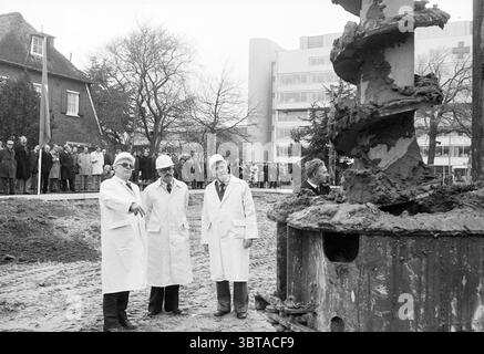 1er message de Hattum et Blankevoort B'wijk premier message, Whizgle News, Dutch Desk, The Netherlands, 1950 - 2000 le 29-01-1978. Ces rubriques apparaissent dans l'image. La scène capture un moment important sur un chantier de construction, où trois hommes en manteaux blancs et casques de sécurité se tiennent bien en vue au premier plan. Leurs expressions attentives suggèrent qu'ils sont engagés dans une discussion sérieuse sur le travail en cours. Une personne fait des gestes vers la machine, indiquant un point d'intérêt ou de préoccupation. En arrière-plan, un groupe de spectateurs – hommes et femmes vêtus de diverses tenues hivernales – se rassemble, obse Banque D'Images