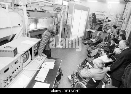 Compagnie de personnes en fauteuil roulant visiter une usine, Whizgle News, Dutch Desk, pays-Bas, 1950 - 2000 sur 10-1987. Ces rubriques apparaissent dans l'image. Dans une pièce bien éclairée, un groupe de personnes s’assoit dans différentes positions, certaines en fauteuil roulant et d’autres debout. Ils se concentrent intensément sur un haut-parleur, un homme âgé avec une barbe, qui se tient près d'une grande machine. Il apparaît animé, faisant des gestes avec ses mains pendant qu'il explique quelque chose, peut-être lié à la machinerie devant lui. La salle est remplie d'une variété d'équipements technologiques, y compris de grands panneaux et des écrans qui font allusion à un complexe Banque D'Images