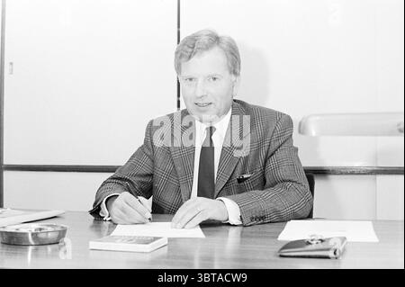 Report HTS Haarlem Report Schools, Whizgle News, Dutch Desk, pays-Bas, 1950 - 2000 on 15-11-1971. Voici les rubriques de l'image. La scène capture un homme assis à un bureau en bois dans un environnement bien rangé. Il a un comportement confiant, vêtu d'une chemise de couleur claire et d'une cravate sombre, complétée par un blazer texturé avec un motif pied-de-poule classique. Ses cheveux sont soigneusement coiffés, et il est concentré sur l'écriture, stylo à la main, comme il se penche légèrement en avant, suggérant l'engagement avec la tâche à accomplir. Le bureau est organisé mais minimaliste, avec quelques feuilles de papier devant lui Banque D'Images