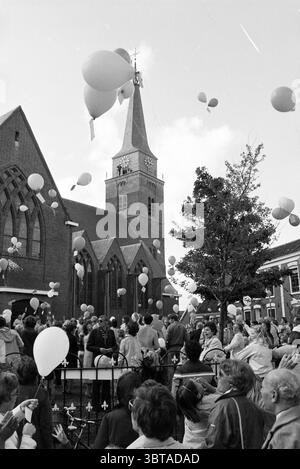 Réouverture de Maartenskerk Hillegom (lâcher des ballons devant l'église), Whizgle News, Dutch Desk, pays-Bas, 1950 - 2000. Ce sont les éléments de l'image. Dans une scène animée en plein air, une grande foule se rassemble devant une impressionnante église en briques avec un grand clocher pointu, marqué par une horloge en son centre. L'architecture de l'église présente des fenêtres cintrées et des détails complexes qui témoignent de son importance historique. Au-dessus de la foule, une multitude de ballons flottent dans le ciel, dont beaucoup sont blancs, créant un contraste fantaisiste avec le ciel couvert en toile de fond. Certains Banque D'Images
