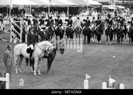 Concours de saut d'obstacles divers Haarlemmermeersebos Haarlemmermeer Haarlemmermeerse Bos, Whizgle News, Dutch Desk, pays-Bas, 1950 - 2000 on 16-06-1990. L'image contient ces rubriques. La scène montre un événement équestre se déroulant dans une arène extérieure vibrante, probablement associée à une atmosphère de foire ou de festival. Au premier plan, un cavalier sur un cheval de couleur claire, son pelage brillant sous la lumière. Le cavalier, vêtu d'une tenue équestre formelle, semble concentré et en contrôle, assis avec confiance au sommet du cheval. A côté d'eux se tient un cheval sombre, tout aussi bien placé, suggérant un M. Banque D'Images