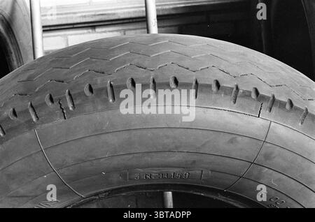 Pneus Noord Zuid Hollandse Vervoersmaatschappij N.V. NZ, Whizgle News, Dutch Desk, pays-Bas, 1950 - 2000 on 07-04-1964. Voici les rubriques de l'image. La scène est dominée par un grand pneu abîmé, sa surface texturée bien en vue. Le pneu présente une sculpture distincte avec des rainures profondes et une légère usure, ce qui indique qu'il a été utilisé de manière significative. Parmi les rainures, de petites fissures bordent la surface, suggérant l'âge et l'usure au fil du temps. Les couleurs sont atténuées, principalement des nuances de noir et de gris variables, avec des reflets qui captent la lumière, révélant les contours du pneu. Banque D'Images
