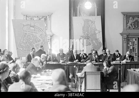 Débat sur le plan structurel de Haarlem conseils municipaux, Whizgle News, Dutch Desk, pays-Bas, 1950 - 2000 le 22-05-1963. Ces rubriques sont illustrées dans l'image. La scène se déroule dans une pièce spacieuse et bien éclairée qui suggère une aura de sérieux et de formalité. Les murs sont ornés de grandes cartes complexes affichées sur des chevalets, offrant des vues détaillées de l'aménagement urbain, suggérant un accent sur la planification ou la gouvernance. Une longue table en bois occupe le centre, entourée d'un groupe diversifié d'individus, chacun engagé dans la discussion. Les participants exposent une gamme d'expressions, de réfléchi co Banque D'Images