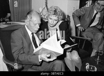 1er exemplaire d'un livre de contes de fées pour Anton Pieck Books and Booksellers, Whizgle News, Dutch Desk, pays-Bas, 1950 - 2000 le 27-09-1984. L'image inclut ces rubriques. Dans un cadre intérieur confortable, deux individus sont assis étroitement ensemble, plongés dans une activité partagée. L'homme âgé, distingué avec des cheveux blancs et vêtu d'un costume, regarde attentivement un livre qu'il tient dans ses mains. Sa tenue se compose d'une cravate sombre contrastant avec une chemise de couleur claire, projetant un air d'autorité et d'expérience. À côté de lui, une femme aux cheveux blonds bouclés se penche, habillée élégamment dans un style aménagé Banque D'Images