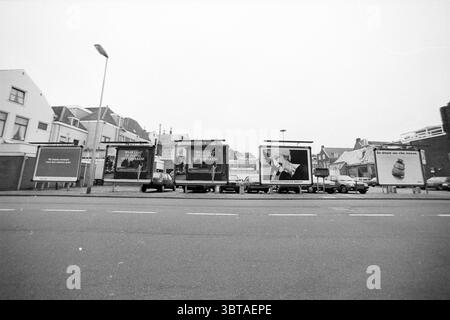 Panneau d'affichage dans la Damstraat Haarlem Damstraat pays-Bas, Whizgle News, Dutch Desk, pays-Bas, 1950 - 2000 le 15-01-1992. L'image montre ces rubriques. Dans cette scène, une série de grands panneaux d'affichage se tiennent en évidence le long d'une rue large, créant un point focal visuel. Les panneaux d'affichage sont remplis d'images diverses, présentant diverses publicités qui attirent l'attention avec leurs conceptions contrastées. Un panneau affiche un portrait saisissant en noir et blanc d'un individu, dont l'expression fait allusion à la pensée profonde ou à l'émotion, tandis qu'un autre affiche des graphiques audacieux dans des couleurs vives que cr Banque D'Images