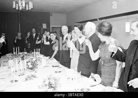 Réception et anniversaire Mr. van Helden Carels Carels réceptions, Whizgle News, Dutch Desk, pays-Bas, 1950 - 2000 le 03-02-1966. Ce sont les éléments de l'image. Dans un cadre bien habillé, les individus se réunissent autour d'une longue table élégamment dressée ornée d'une nappe blanche éclatante. La table est décorée avec des arrangements floraux avec des tons doux de rose et de jaune, ajoutant une touche d'élégance à la scène. Le groupe, habillé en tenue formelle, comprend des hommes et des femmes, debout épaule contre épaule alors qu'ils lèvent leurs lunettes en portant un toast. Leurs expressions sont joyeuses et célébrités Banque D'Images