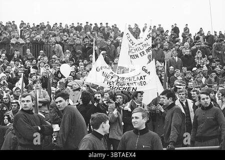 Vorwärts Berlin - Feyenoord Football Feijenoord, Whizgle News, Dutch Desk, pays-Bas, 1950 - 2000 le 04-03-1970. L'image montre ces rubriques. La scène capture une grande foule réunie dans un stade ou une zone ouverte, principalement remplie de jeunes adultes et d'adolescents. Ils semblent participer à une manifestation ou à un rassemblement animés, comme en témoignent les nombreuses pancartes et banderoles tenues haut au-dessus de la foule. L'atmosphère est chargée d'un sentiment d'urgence et d'enthousiasme. Beaucoup de gens au premier plan sont habillés de vêtements simples et sombres, ce qui contribue à une palette monochrome globale Banque D'Images