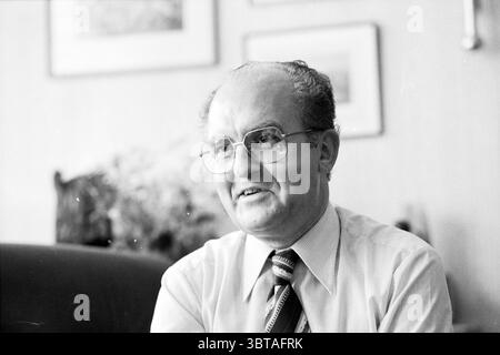 Portrait de Dean Peters Portraits Église catholique romaine, Whizgle News, Dutch Desk, pays-Bas, 1950 - 2000 le 18-08-1981. Ces rubriques sont illustrées dans l'image. Un homme d'âge moyen est assis dans une position détendue, véhiculant un comportement de chaleur et d'accessibilité. Il a un sourire doux et porte de grandes lunettes à la mode qui ajoutent une touche savante à son apparence. Ses cheveux sont soigneusement peignés et légèrement amincis, suggérant un style classique d'une époque antérieure. Il est habillé d'une chemise boutonnée de couleur claire avec un col, jumelé avec une cravate rayée qui incorpore des nuances de bleu et Banque D'Images