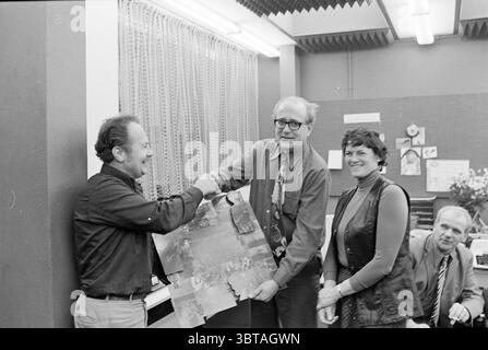 Adieu Mr. Wetzelaar sur IJmuider courant People journaux et magazines, Whizgle News, Dutch Desk, pays-Bas, 1950 - 2000 on 03-12-1976. Ces rubriques sont illustrées dans l'image. Dans un cadre intérieur bien éclairé, quatre personnes participent à un moment de célébration ou de reconnaissance. L'arrière-plan présente un mur orné de divers documents et matériaux visuels, probablement révélateur d'un espace de travail créatif ou professionnel. À gauche, un homme avec une apparence soignée serre la main à un autre homme qui tient une grande pièce visuelle, peut-être une affiche ou une grande photographie. Le Banque D'Images