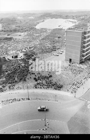 Extension de routes IJmuiden Road construction de routes plantation de routes, Whizgle News, Dutch Desk, pays-Bas, 1950 - 2000 le 13-08-1970. L'image montre ces rubriques. La scène présente un vaste paysage qui fusionne des éléments naturels et urbains. Au premier plan, une route sinueuse courbe doucement, son asphalte noir contrastant avec le terrain environnant. Une voiture solitaire se déplace le long de la route, indiquant un sens du mouvement et peut-être la solitude dans ce cadre expansif. À gauche, une parcelle de basse verdure et d'arbustes clairsemés s'étend vers l'horizon, créant un tampon naturel contre l'éléme urbain Banque D'Images