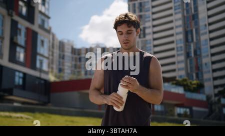Homme caucasien athlète masculin Guy sport boire bouteille d'eau rafraîchir la ville d'entraînement en dehors du coureur de fitness sportif sain bien-être de santé assoiffé Banque D'Images
