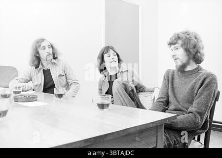 Jeunes à la table, Whizgle News, Dutch Desk, pays-Bas, 1950 - 2000 le 26-09-1974. L'image inclut ces rubriques. Dans une salle modeste et légèrement éclairée, trois personnes sont assises à une grande table en bois au fini chaud et poli. Le cadre présente des murs de couleur neutre qui améliorent la simplicité de l'espace. À gauche, un homme aux cheveux longs et bouclés et à la moustache épaisse est habillé de façon décontractée dans une chemise boutonnée. Il affiche une expression de contemplation réfléchie en regardant légèrement sur le côté. À côté de lui se trouve une femme aux cheveux foncés à la longueur des épaules, portant un noir ajusté Banque D'Images