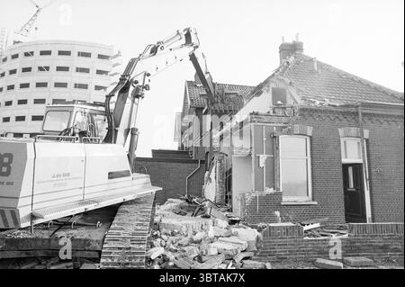 Mur de palplanches + démolition à la tête du port IJmuiden IJmuiden pays-Bas, Whizgle News, Dutch Desk, pays-Bas, 1950 - 2000 on 28-11-1993. Voici les rubriques de l'image. La scène présente un chantier de construction où une pelle de machinerie lourde démolit activement un bâtiment. La pelle, peinte dans un schéma de couleurs blanc et orange audacieux, se tient puissamment au premier plan, son bras étendu avec un grand godet positionné près de la structure exposée du bâtiment. Le bâtiment, une fois une maison, apparaît partiellement intact mais s'effrite considérablement d'un côté, révélateur Banque D'Images