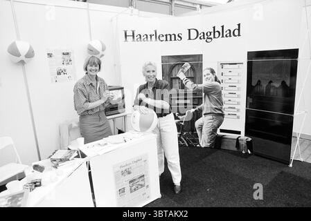 Stand Haarlems Dagblad Lentebeurs, Whizgle News, Dutch Desk, pays-Bas, 1950 - 2000 le 18-05-1992. L'image montre ces rubriques. La scène capture un espace d'exposition vibrant et animé. Deux personnes se tiennent bien en vue sur un stand d'exposition, à la fois souriant et engageant avec le spectateur, créant une atmosphère accueillante. Une personne, vêtue d'une blouse à carreaux, a un comportement expressif, tandis que l'autre, dans une chemise sombre, semble détendue et confiante. L'arrière-plan de la cabine comporte un grand mur orné de graphiques et d'images, y compris une photographie montrant quelqu'un qui interagit activement w Banque D'Images