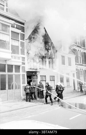 Incendie Haymarket Fire brigade Haarlem Hooimarkt pays-Bas, Whizgle News, Dutch Desk, pays-Bas, 1950 - 2000 on 26-06-1980. L'image inclut ces rubriques. La scène se déroule dans un environnement urbain caractérisé par une rangée de bâtiments, dont l'un en particulier montre des signes de dégâts importants. La structure endommagée semble avoir été engloutie dans les flammes, alors que la fumée s'écoule de ses niveaux supérieurs, créant un contraste frappant avec le ciel dégagé. La façade de ce bâtiment, autrefois probablement vibrante, révèle désormais du bois carbonisé et des fenêtres brisées. Les pompiers sont activement engagés dans la lutte Banque D'Images