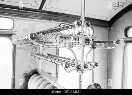 Wagon ferroviaire restauré + hr. Karskens Treinen, Whizgle News, Dutch Desk, pays-Bas, 1950 - 2000 sur 12-04-1977. L'image montre ces rubriques. La scène capture l'intérieur d'un chariot de transport vintage, avec des étagères métalliques suspendues au plafond. Ces casiers sont conçus avec une série de barres horizontales et un filet qui permet de ranger les effets personnels des passagers. La surface des éléments métalliques luit subtilement, indiquant qu'ils sont bien entretenus, bien que suggérant leur âge. Le chariot est principalement orné de nuances de gris doux et de crème, évoquant un nostalgique AT Banque D'Images