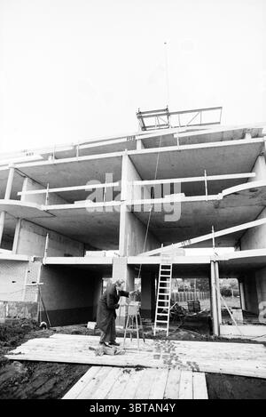 Point culminant de Badhoevedorp Badhoevedorp, Whizgle News, Dutch Desk, pays-Bas, 1950 - 2000 on 19-10-1992. Voici les rubriques de l'image. Dans la scène, un chantier de construction est mis en évidence, mettant en vedette une structure partiellement construite avec plusieurs niveaux. Le bâtiment est composé de béton, mettant en valeur sa texture brute et industrielle. Le cadre révèle des espaces vides où les fenêtres seront éventuellement installées, et certaines zones sont encore bordées d'échafaudages, indiquant une construction active. Une figure se tient au premier plan, concentrée intentionnellement sur un petit chevalet. Cette personne est habillée Banque D'Images