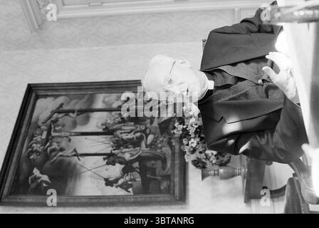 Mgr. Lescrauwaet, Whizgle News, Dutch Desk, pays-Bas, 1950 - 2000 on 16-10-1991. Ces rubriques apparaissent dans l'image. La scène montre un homme plus âgé assis à une table, sa tenue se caractérise par un vêtement sombre qui suggère un rôle clérical. Ses cheveux sont blancs et soigneusement peignés, et il porte des lunettes qui accentuent son expression réfléchie. L'homme semble engagé dans la conversation ou la pensée profonde, ses mains faisant des gestes expressifs, comme s'il véhiculait un point important. En arrière-plan, une grande peinture domine le mur, représentant une scène dramatique remplie de figures humaines. Le Banque D'Images