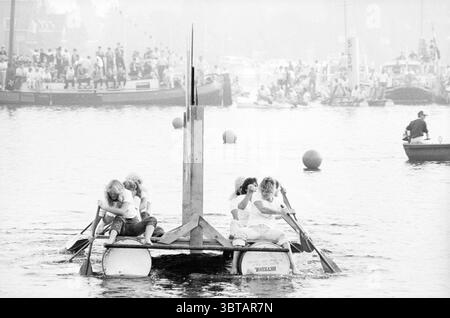 Course de radeau Vijfhuizen compétitions Vijfhuizen, Whizgle News, Dutch Desk, pays-Bas, 1950 - 2000 le 12-09-1985. Ces rubriques sont illustrées dans l'image. La scène capture un événement aquatique animé avec un sentiment de camaraderie et de compétition. Au premier plan, un radeau de fortune est vu, fabriqué à partir de poutres en bois et de tonneaux. Quatre individus, habillés de hauts blancs assortis et de bas foncés, aviron énergiquement, leurs expressions étant un mélange de concentration et de détermination alors qu'ils travaillent à l'unisson. L’orientation de leur corps pointe vers l’horizon, attirant le regard du spectateur vers l’avant. Le dos Banque D'Images