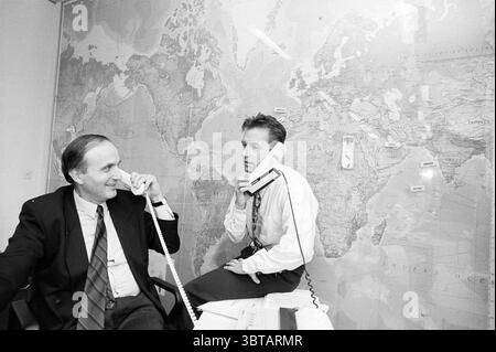 Deux messieurs de ITC Haarlem Haarlem pays-Bas, Whizgle News, Dutch Desk, pays-Bas, 1950 - 2000 le 23-03-1994. Ces rubriques sont illustrées dans l'image. Dans un environnement de bureau animé, deux hommes sont engagés dans une conversation tout en utilisant le téléphone. La toile de fond présente une grande carte du monde qui couvre presque tout le mur, mettant en évidence divers pays et continents avec un éventail de couleurs, y compris des nuances de bleu, vert et brun. Un homme, assis à un bureau, est habillé d'un costume formel et d'une cravate qui contraste fortement avec les tons neutres du bureau. Son expression transmet un mi Banque D'Images