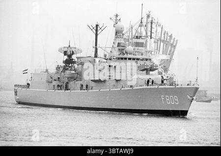 Navires de guerre à IJmuiden navires IJmuiden pays-Bas, Whizgle News, Dutch Desk, pays-Bas, 1950 - 2000 le 28-04-1980. Ce sont les éléments de l'image. La scène représente un navire de la marine se déplaçant gracieusement dans l'eau, sa coque peinte dans une couleur grise sourde qui complète l'atmosphère brumeuse qui l'entoure. Ce navire, avec sa conception simplifiée, présente diverses caractéristiques militaires, y compris des systèmes radar et des antennes au sommet du pont. Le cadre est industriel, faisant allusion à un port ou à une zone portuaire avec des grues et des conteneurs de fret visibles en arrière-plan, bien que légèrement masqués par Banque D'Images