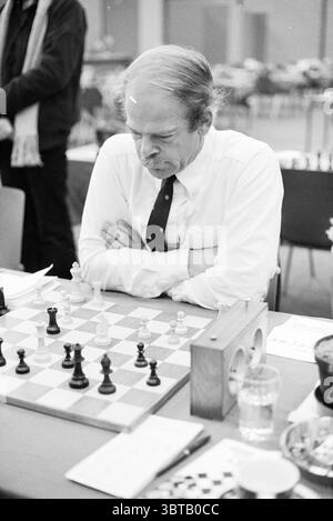 Parlementaires joueurs d'échecs tournoi d'échecs de Hoogovens 1980 Wijk aan Zee, Whizgle News, Dutch Desk, pays-Bas, 1950 - 2000 on 19-01-1980. Voici les rubriques de l'image. La scène représente un individu réfléchi assis à un échiquier, profondément engagé dans la contemplation. La personne a une apparence distinguée avec des cheveux grisâtres et est habillée d'une chemise blanche jumelée à une cravate sombre, exsudant un sentiment de sérieux et de concentration. L'échiquier, situé au centre, présente un arrangement classique des pièces, avec un contraste net entre les figures noires et blanches. Les pièces noires sont bol Banque D'Images