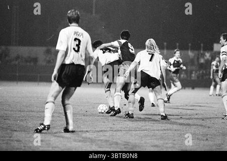 Haarlem - Veendam, Whizgle News, Dutch Desk, pays-Bas, 1950 - 2000 le 25-09-1992. L'image inclut ces rubriques. La scène capture un moment intense sur un terrain de football, sous la faible lueur des projecteurs du stade qui projettent de longues ombres sur l'herbe. Les joueurs sont en mouvement, engagés dans un affrontement compétitif pour la possession d'un ballon de football. Au premier plan, deux joueurs sont enchevêtrés ; l'un, vêtu d'un maillot sombre portant le numéro 9, pousse contre l'autre portant un maillot léger, marqué du numéro 7. Leur concentration et leur détermination sont évidentes lorsqu'ils exercent un effort physique. Banque D'Images