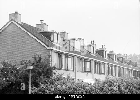 Dormer Windows Hoofddorp pays-Bas, Whizgle News, Dutch Desk, pays-Bas, 1950 - 2000 le 01-06-1990. Ce sont les éléments de l'image. La scène capture une rangée de maisons résidentielles, chacune avec un style architectural distinct caractérisé par un toit en pente et de charmantes lucarnes jetant un coup d'œil d'en haut. Les bâtiments sont construits en brique, présentant une palette discrète de gris doux et de tons terreux, qui se marient harmonieusement avec l'environnement. Au premier plan, une végétation luxuriante enveloppe la base des maisons, avec un buisson dense qui ajoute de la texture et de la profondeur à la scène. Banque D'Images