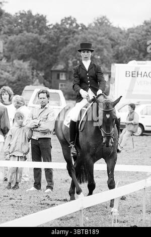 Dressage Mrs. Gaastra - R@@, Whizgle News, Dutch Desk, pays-Bas, 1950 - 2000 le 26-08-1995. L'image inclut ces rubriques. La scène présente un événement équestre animé, sur fond d'herbe verte et d'arbres. Au centre, une cavalière en tenue habillée, avec une veste noire ajustée, des culottes blanches et un grand chapeau d'équitation noir, attire l'attention alors qu'elle s'assoit gracieusement sur son cheval bien entretenu, qui est une nuance de brun profond. Le cheval semble calme et bien fixé, son manteau brillant reflétant la lumière du ciel couvert. Autour du cavalier, une petite foule de spectateurs observe Banque D'Images