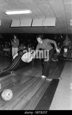 Compétition de bowling., Whizgle News, Dutch Desk, pays-Bas, 1950 - 2000. L'image contient ces rubriques. Dans un cadre de bowling animé, un homme est prêt à l'action, capturé à mi-course avec une attention particulière sur la balle de bowling qui glisse sur la piste. Il porte une chemise en noir et blanc à motifs, son design tourbillonnant offrant un contraste saisissant avec la ruelle en bois lisse sous lui. Son pantalon est sombre, bien ajusté lorsqu'il se penche en avant, incarnant la concentration et la détermination. En arrière-plan, l’atmosphère est remplie d’un mélange d’énergie et d’anticipation. Une petite foule de spectateurs est g Banque D'Images