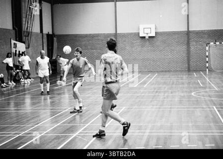 Tournoi de football en salle Zeewijkhal IJmuiden Football en salle IJmuiden pays-Bas, Whizgle News, Dutch Desk, pays-Bas, 1950 - 2000 on 20-06-1989. Ces rubriques sont illustrées dans l'image. La scène représente une activité sportive intérieure se déroulant dans un gymnase spacieux. Le sol, en bois poli, reflète la lumière ambiante et révèle une série de lignes blanches marquant les limites de la cour. Les murs sont ornés d'une texture de briques chaleureuse et terreuse qui ajoute à l'atmosphère chaleureuse de l'environnement. Au premier plan, deux jeunes athlètes s’engagent dans un jeu animé impliquant un ballon. Un Banque D'Images
