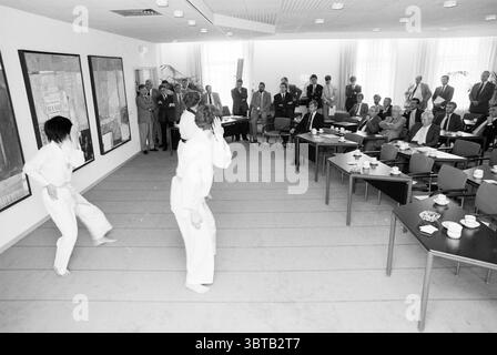 Réunion du Dutch Korean Trade Club incluant une démonstration de taekwondo, Whizgle News, Dutch Desk, pays-Bas, 1950 - 2000 le 14-09-1989. Ces rubriques apparaissent dans l'image. La scène capture un cadre intérieur formel, probablement une salle de conférence ou un environnement similaire. Les murs sont ornés de grandes œuvres d'art abstraites qui introduisent des couleurs vives telles que les rouges, les bleus et les jaunes, offrant un contraste frappant avec la pièce aux tons neutres. Au premier plan, deux individus sont engagés dans une démonstration d'arts martiaux, vêtus de GI blanc traditionnel. Leurs mouvements sont dynamiques et précis, Banque D'Images