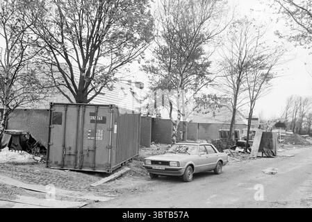 Arbres dans la nouvelle construction min. Van Houtenlaan IJm. Arbres IJmuiden Ministre van Houtenlaan pays-Bas, Whizgle News, Dutch Desk, pays-Bas, 1950 - 2000 on 27-10-1980. Voici les rubriques de l'image. La scène présente un cadre urbain un peu désolé caractérisé par un mélange d'éléments industriels et résidentiels. Un grand conteneur d'expédition, peint en bleu pâle, se trouve bien en vue sur le bord de la route. Autour de lui se trouvent des restes dispersés de l'activité humaine : des tas de débris et des objets jetés font allusion à la négligence, avec un sentiment général d'encombrement. Au premier plan, un millésime Banque D'Images