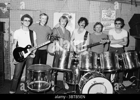 Pop Group Out of Reach Music, Whizgle News, Dutch Desk, pays-Bas, 1950 - 2000 sur 14-03-1981. Ce sont les éléments de l'image. Dans un cadre intérieur animé, un groupe de six musiciens se tient debout, rayonnant un sentiment de camaraderie et d'énergie. L'espace est légèrement sombre, avec des textures du mur et du fond offrant une sensation rustique. Les individus sont divers dans l'apparence et la tenue : deux membres tiennent des guitares ; l'un dispose d'une guitare électrique noire élégante, tandis que l'autre présente une guitare basse. Le guitariste à gauche est habillé de façon décontractée avec des lunettes et une posture confiante. Banque D'Images