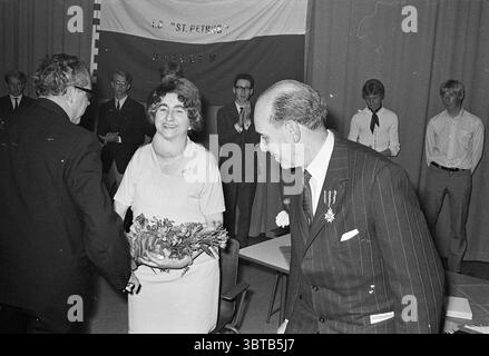 Honoring Mr. Rosenthal Homage, Whizgle News, Dutch Desk, pays-Bas, 1950 - 2000 on 25-06-1969. Ces rubriques sont illustrées dans l'image. Dans un cadre intérieur formel, plusieurs personnes sont rassemblées, créant un sentiment d'occasion. L’atmosphère est remplie d’un mélange de joie et de formalité. Au premier plan, une femme aux cheveux bouclés est vue souriant chaleureusement alors qu'elle reçoit un bouquet de fleurs, sa tenue subtilement élégante. Elle est positionnée au centre, attirant l'attention avec son expression rayonnante. À sa gauche, un homme en costume sombre étend sa main dans un geste de salutation, signifiant probablement apprécier Banque D'Images