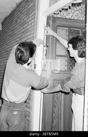 Campagne bricoleur IJmond MTS Schools, Whizgle News, Dutch Desk, pays-Bas, 1950 - 2000 le 21-12-1984. L'image contient ces rubriques. Dans un cadre intérieur confortable, deux individus sont engagés dans une tâche collaborative. Les murs sont ornés d'un motif de briques texturées, prêtant un charme rustique à l'espace. La lumière naturelle filtre à travers une fenêtre voisine, projetant des ombres douces et éclairant la scène d'une lueur chaude. Une personne se tient à gauche, concentrée intensément sur un outil, probablement un appareil de mesure, tenu dans ses mains. Cet individu porte un pull de couleur claire, le tissu apparaissant s Banque D'Images