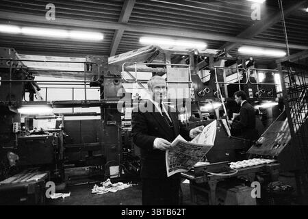 Ton van Groeningen Nieuw Vennep Nieuw-Vennep, Whizgle News, Dutch Desk, pays-Bas, 1950 - 2000 on 25-11-1991. L'image montre ces rubriques. Dans la scène, une imprimerie animée est vivante avec l'activité. Au centre de la composition se trouve un homme d'âge mûr, vêtu d'un costume sombre et d'une cravate, qui sourit alors qu'il tient un grand journal imprimé. Son expression exprime de la fierté et de l'enthousiasme pour le travail qui est fait autour de lui. En arrière-plan, les presses à imprimer massives dominent l'espace, leurs tons gris et argent industriels créant un contraste frappant avec l'aspect chaleureux et invitant de th Banque D'Images