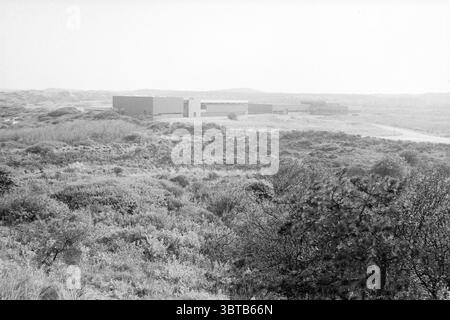 Water Company Pumping station Wijk aan Zee Waterworks Wijk aan Zee, Whizgle News, Dutch Desk, pays-Bas, 1950 - 2000 on 05-05-1989. Ces rubriques apparaissent dans l'image. La scène représente un vaste paysage caractérisé par un terrain doux et vallonné. Au premier plan dominent des taches de hautes herbes et des arbustes bas qui créent une couche texturée de teintes vertes et brunes, évoquant la beauté naturelle de la région. La vie végétale semble luxuriante et quelque peu sauvage, se mélangeant harmonieusement avec l'environnement. Au milieu, on peut voir une série de structures modernes, leurs lignes épurées et leurs géométries Banque D'Images