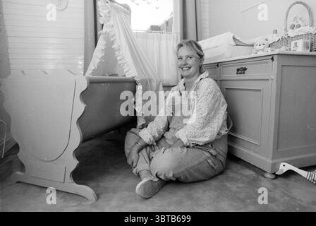 Jeanine Verhagen enceinte, Whizgle News, Dutch Desk, pays-Bas, 1950 - 2000 on 10-05-1990. Ce sont les éléments de l'image. Dans une pépinière confortable et doucement éclairée, une femme est assise avec satisfaction sur le sol recouvert de moquette, ses jambes croisées confortablement devant elle. Elle porte une combinaison de couleur claire sur une blouse à manches longues et motifs, qui ajoute une touche décontractée mais chaude à son apparence. Ses cheveux sont portés dans un style détendu, et un doux sourire orne son visage, véhiculant une humeur de bonheur et de tranquillité. Autour d'elle, la pépinière est ornée de tons pastel, principalement bleus doux et blancs, Banque D'Images