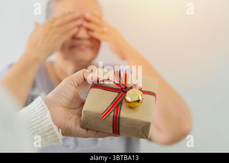 Plan de la main de la fille tenant et donnant cadeau surprise à la mère aînée à noël. Mise au point sélective. Banque D'Images