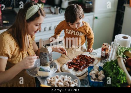 Mère et enfant faisant une pizza maison ensemble dans une cuisine confortable Banque D'Images
