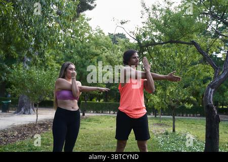 Homme et femme s'échauffant ensemble dans un parc, effectuant des étirements de bras avant de commencer leur routine d'entraînement Banque D'Images